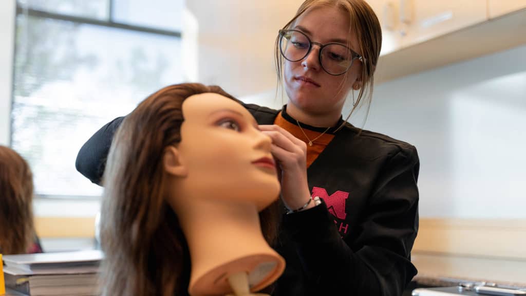 Cosmetology student styling mannequin hair