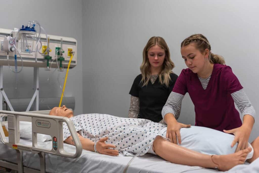Two nursing assistant students helping a training manikin