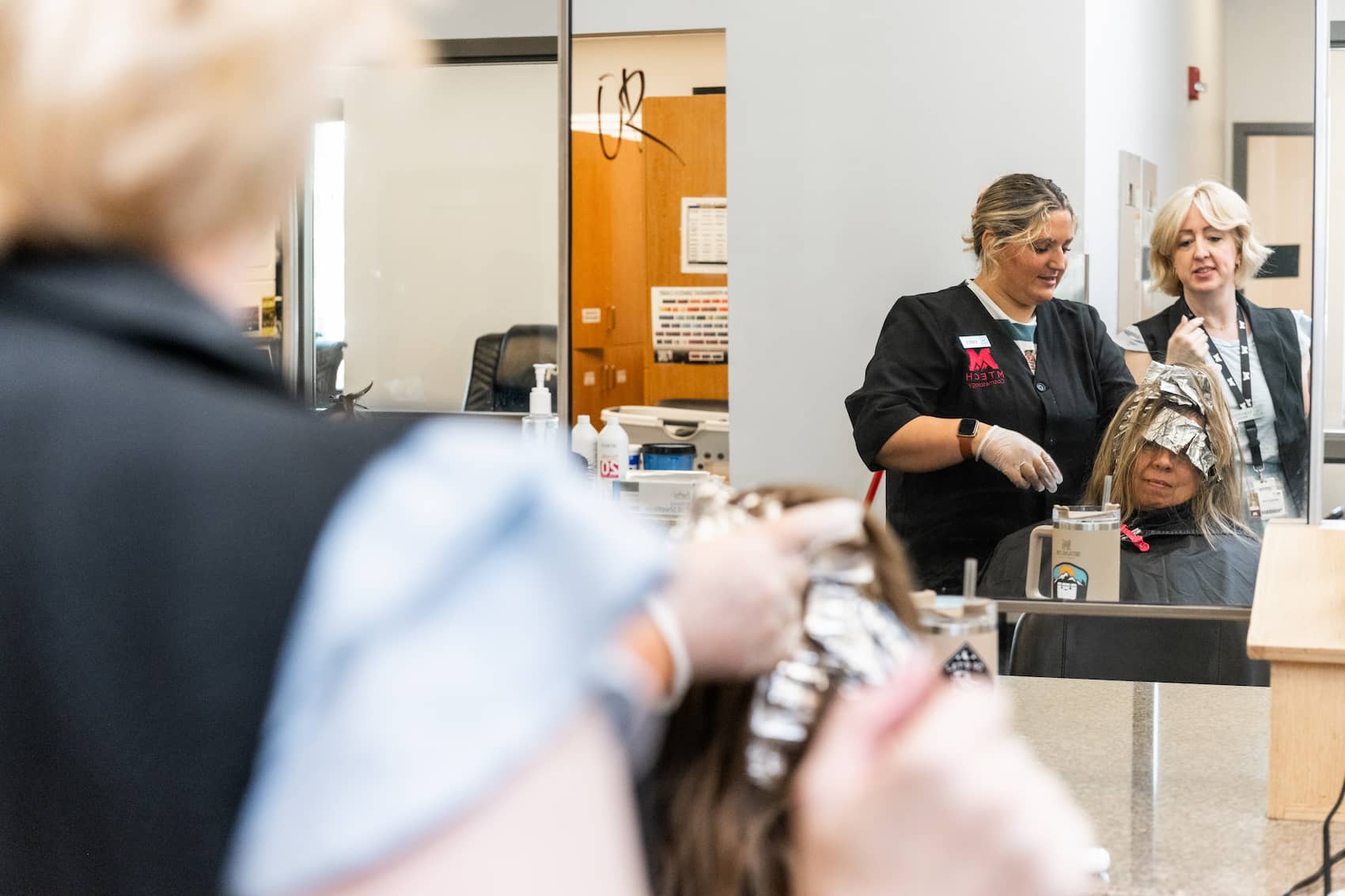 Student applying hair dye to customer with instructor supervision