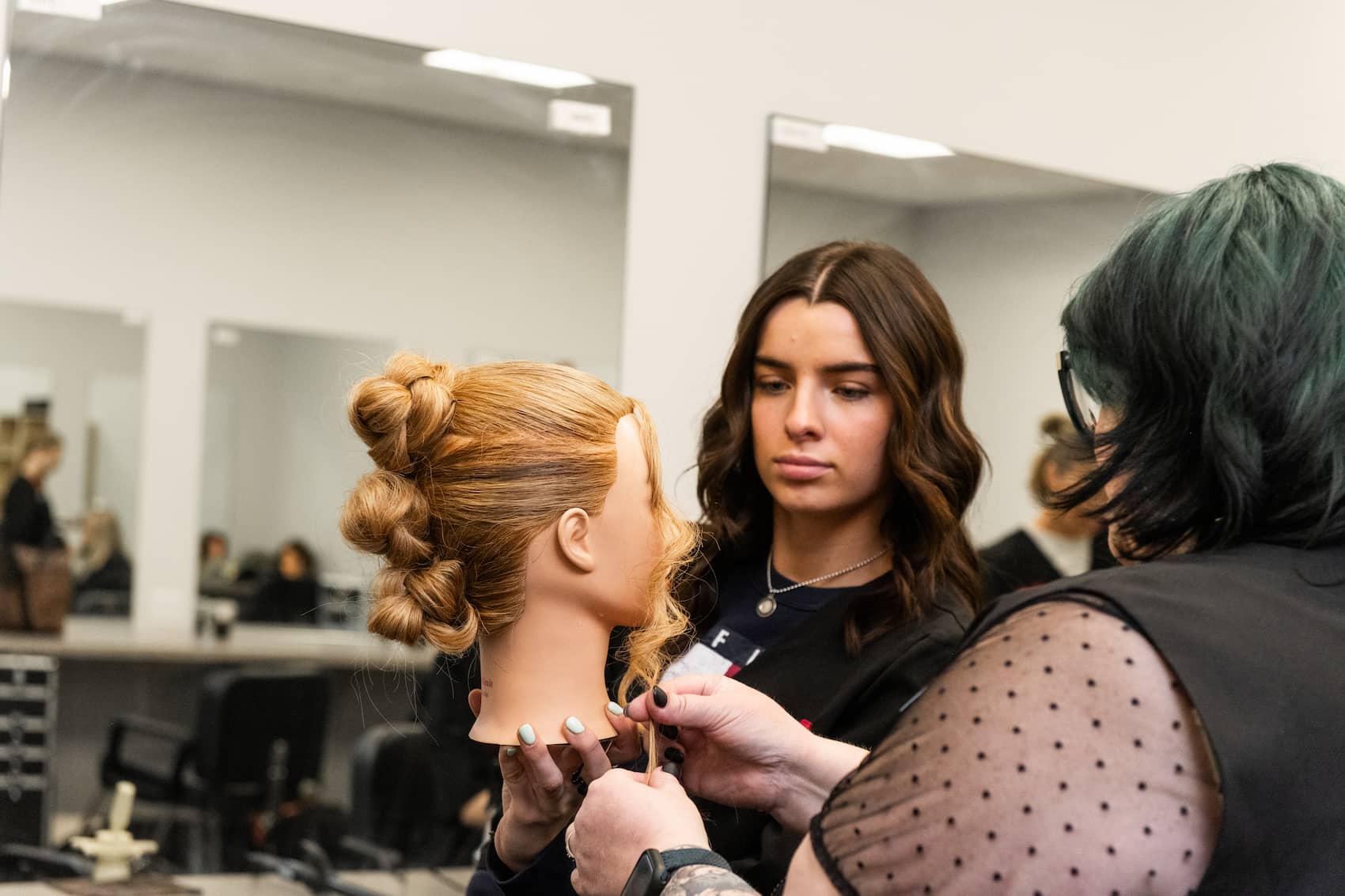 Student curling mannequin's hair with help from instructor