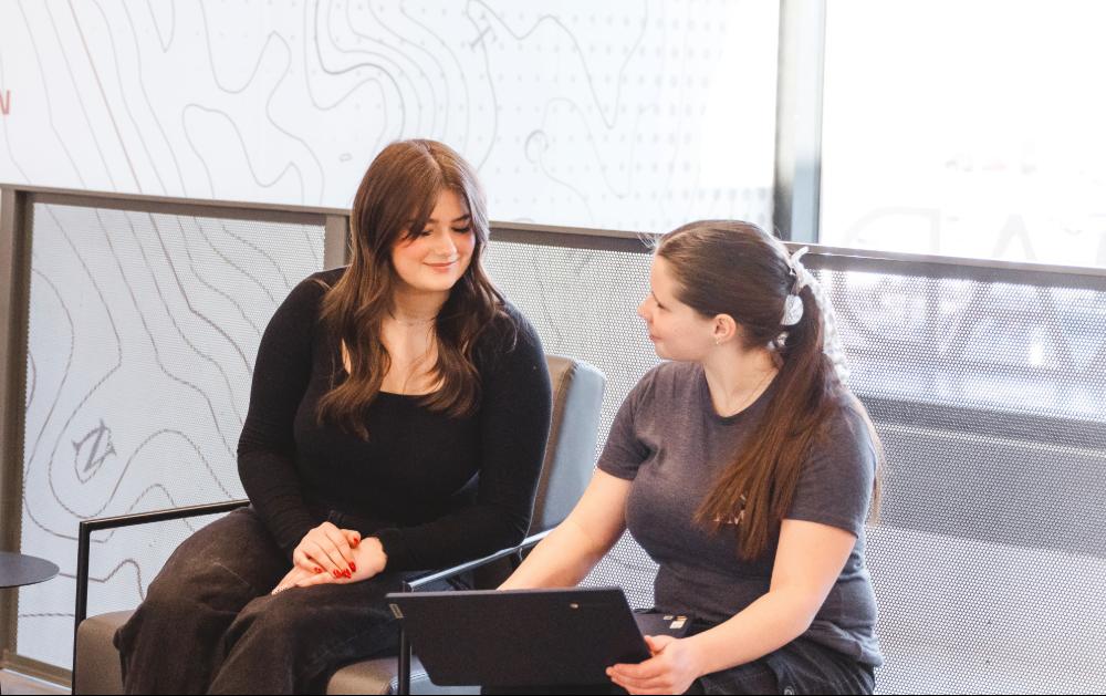 Two students look at a laptop in the hallway